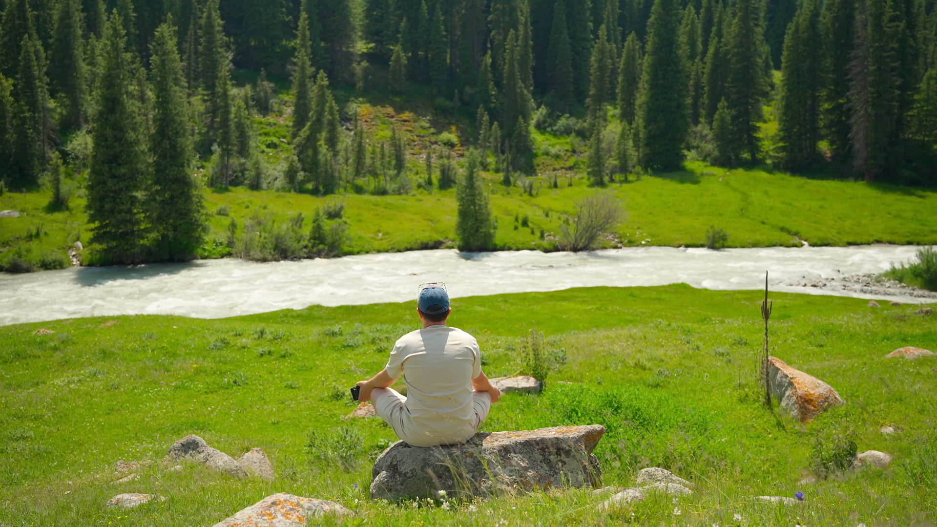 Man relaxing by a mountain river during a self-drive trip in Kyrgyzstan